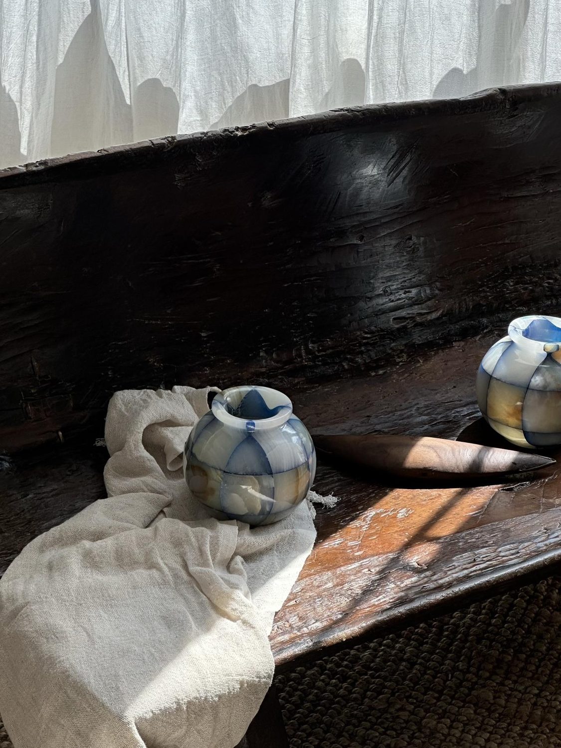 A banded blue stone vase on a dark wooden table beside draped linen.