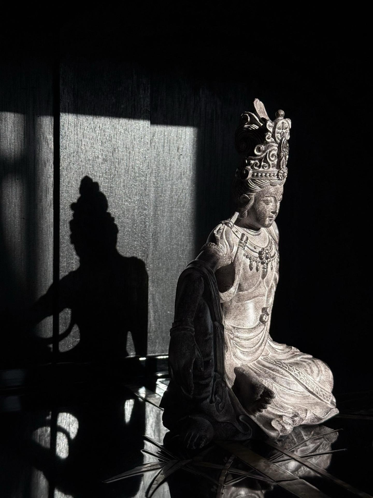 A carved stone bodhisattva seated in shadow, a beam of afternoon light falling across a linen wall.